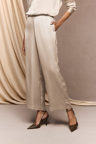 Angled front view of the elegant satin trousers with pockets in front of a champagne background #color_champagne