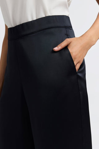 Close up side view of elegant satin fabric and elastic waistband with models hand in the functioning pocket #color_black