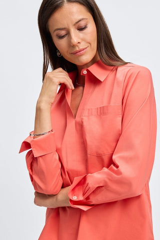 Waist up view of woman wearing the Bella No Iron Stretch Long Sleeve Shirt
with the cuffs folded up #color_tangerine