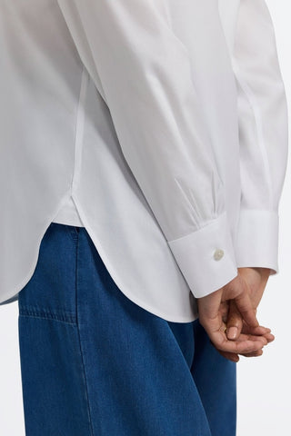 Side view of women wearing the Meghan No Iron Pinpoint Long Sleeve Shirt untucked with her hands behind her back #color_white