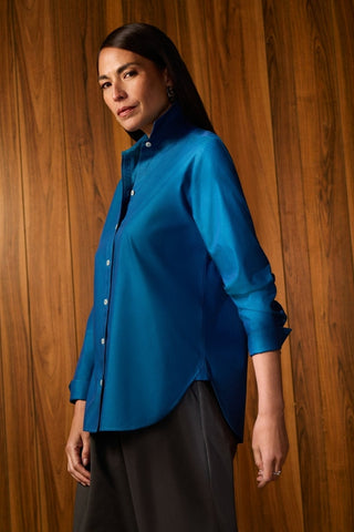 Angled side view of woman wearing the Meghan No Iron Pinpoint Long Sleeve Shirt with a wooden background #color_teal