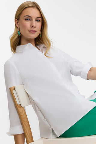 Angled front view of model sitting in chair wearing the Beatrice Pearl Stretch Matte Sateen 3/4 Sleeve Shirt with green pants #color_white