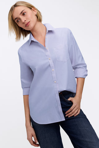 Angled front view of woman wearing the Boyfriend No Iron Pinpoint Long Sleeve Tunic with folded sleeves and one side tucked into her pants #color_blue wave